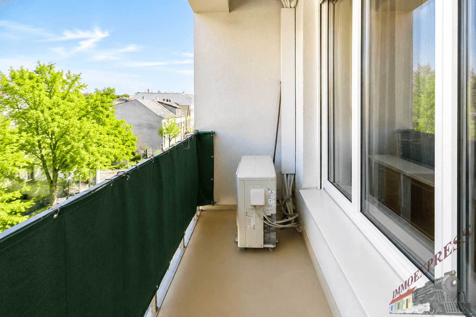 Schmaler Balkon mit grüner Sichtschutzwand und einer Klimaanlage im Freien.