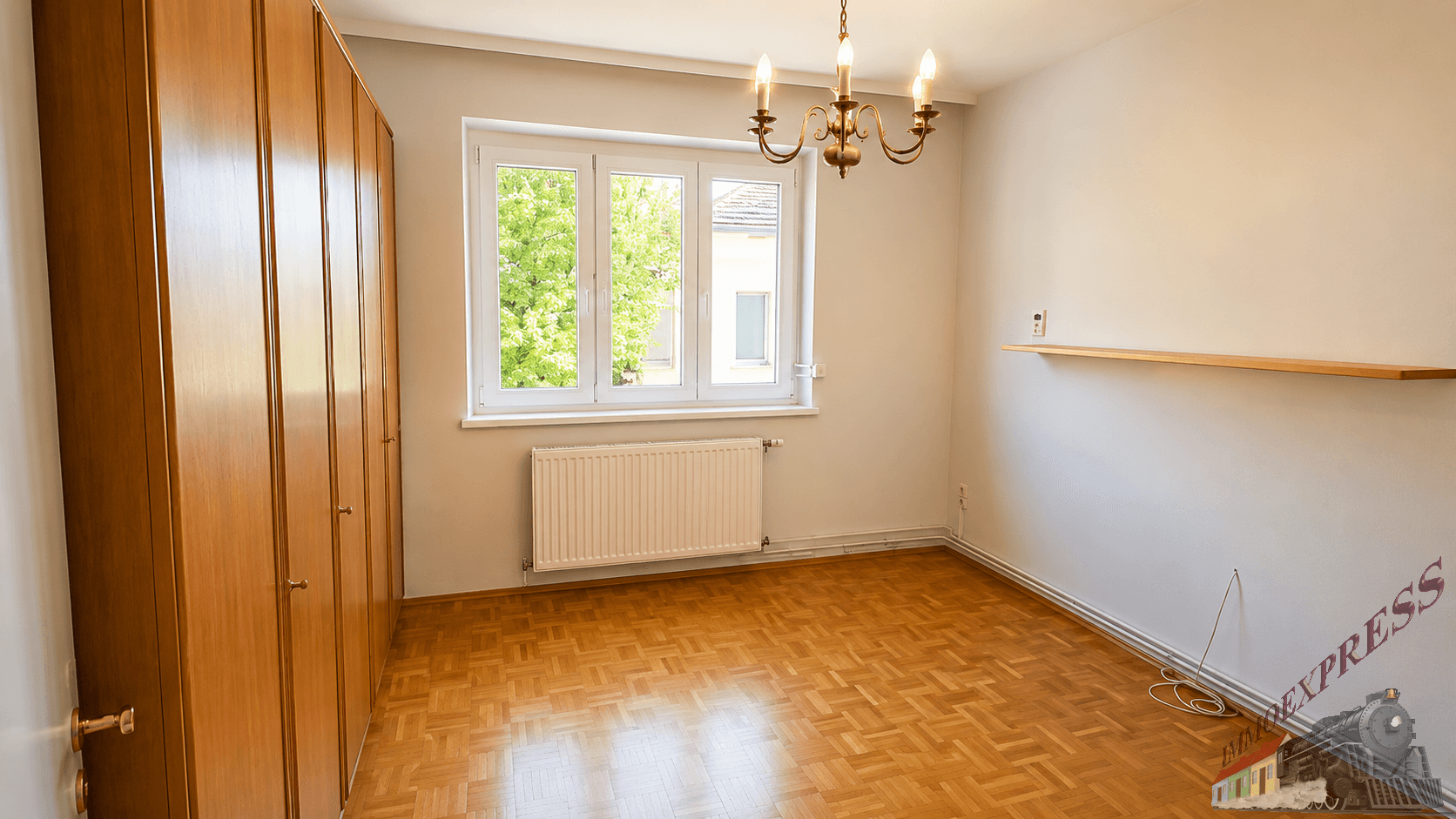 Schlafzimmer mit Parkettboden, großem Holzschrank und Fenster mit Blick ins Grüne.