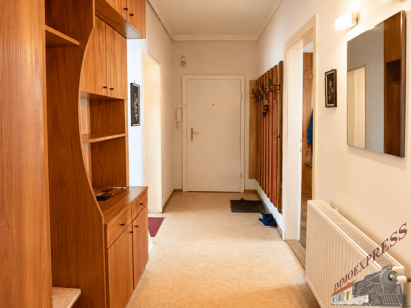 Geräumiger Eingangsbereich mit Holzmöbeln und Garderobe, der zur Wohnungstür führt.