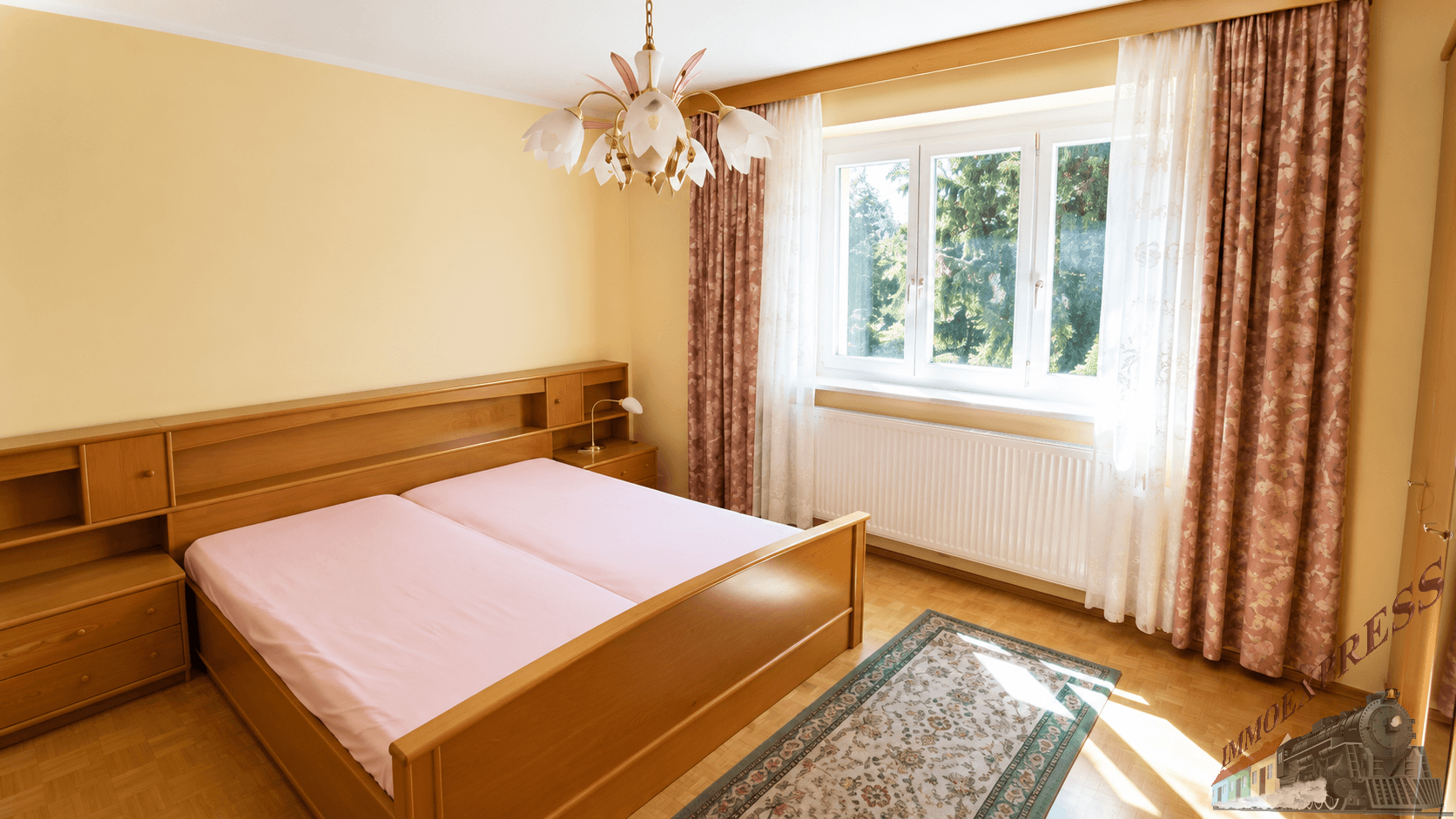 Helles Schlafzimmer mit Doppelbett aus Holz und großem Fenster mit Blick ins Grüne.