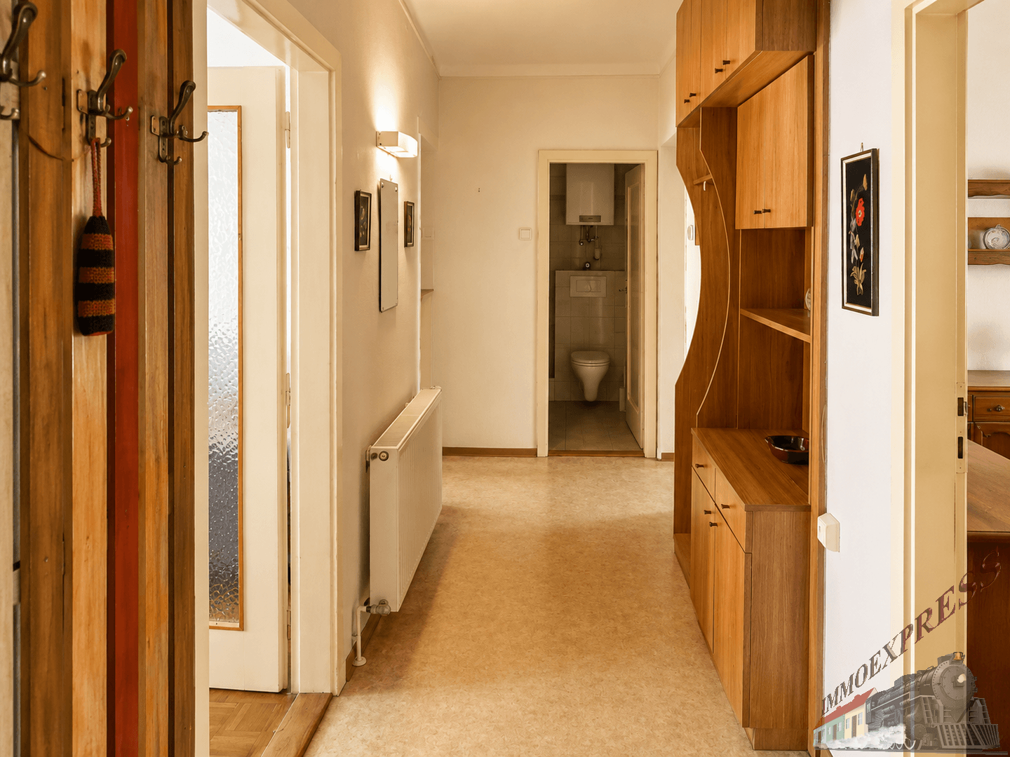Heller Flur mit praktischen Holzmöbeln und Garderobe, der zu einem kleinen Gäste-WC führt.