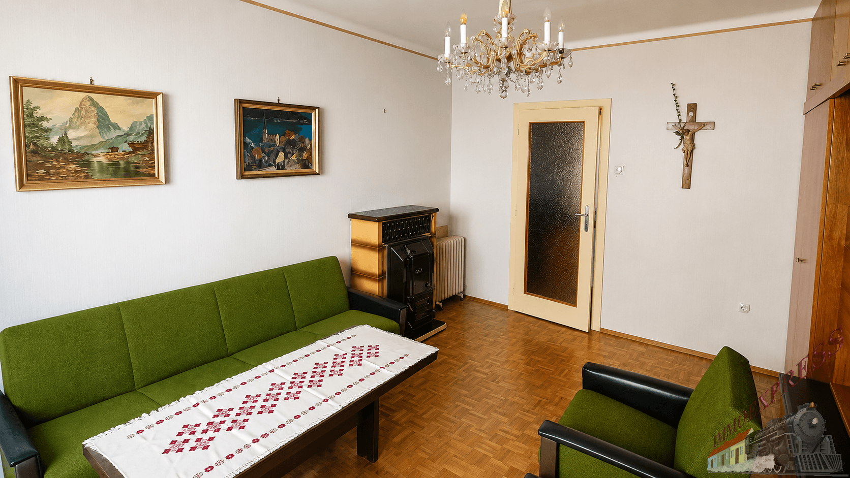 Traditionelles Wohnzimmer mit grünem Sofa, Kachelofen und Kronleuchter, dekoriert mit klassischen Gemälden.