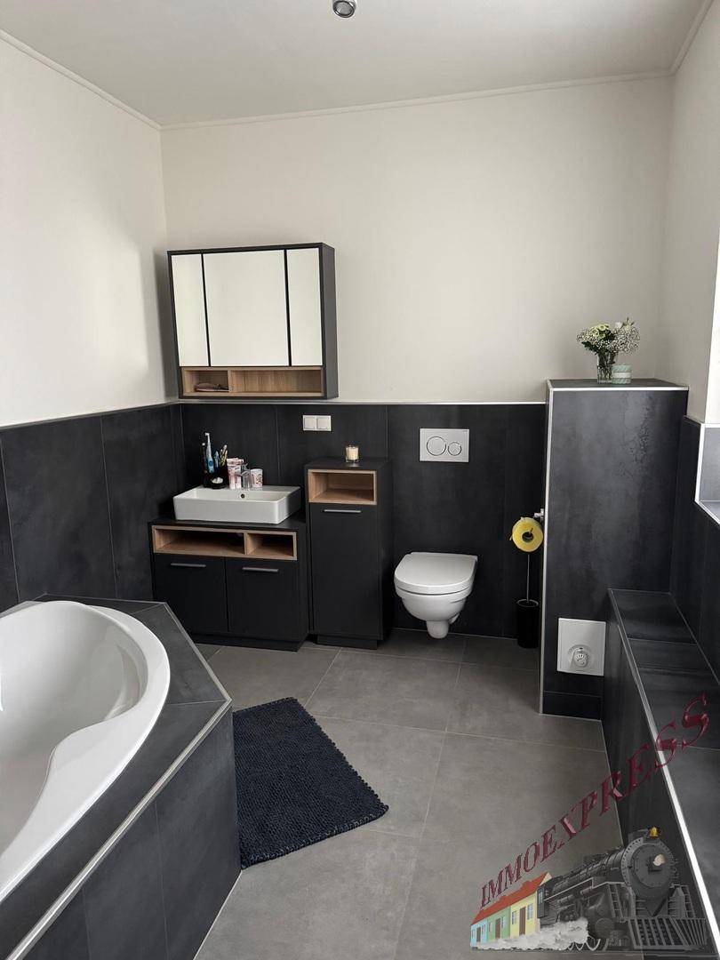 Modernes Badezimmer mit Badewanne, wandhängendem WC und dunklen Fliesen.