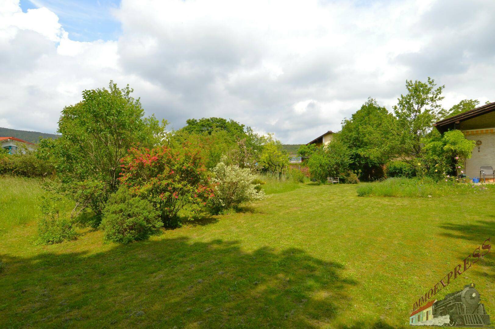 Panoramablick auf das Haus und den weitläufigen Garten mit vielfältiger Bepflanzung.