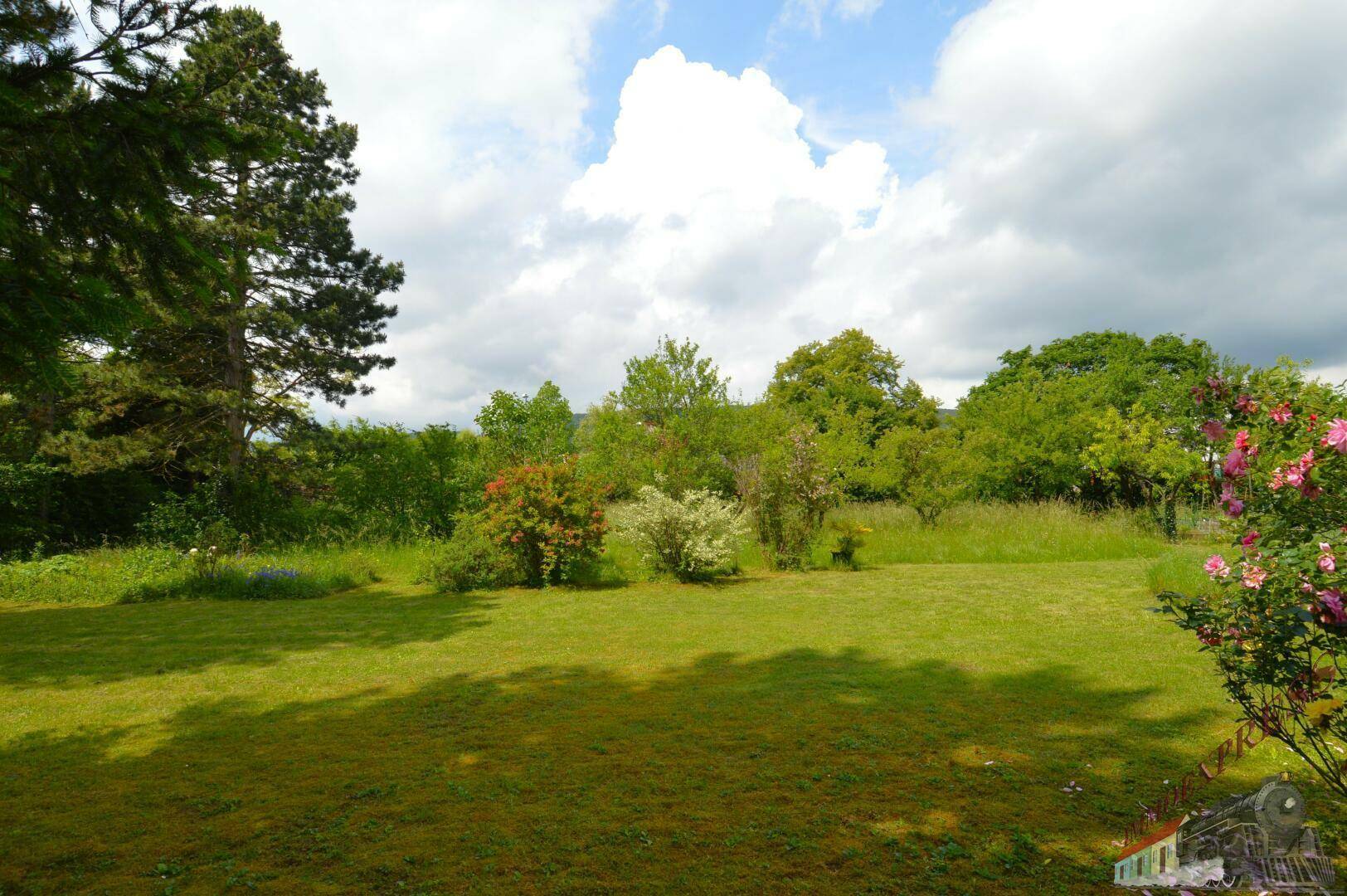 Weitläufiger Garten mit üppigem Grün, Bäumen und Sträuchern unter einem bewölkten Himmel.
