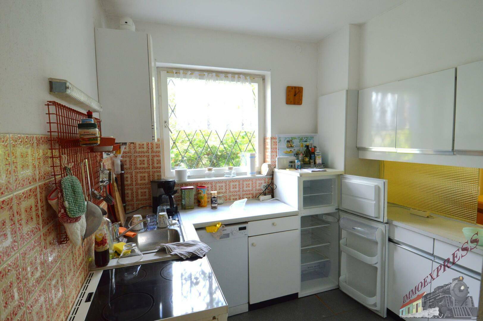 Funktionale Küche mit weißen Schränken, Spüle und Fenster mit Blick ins Grüne.