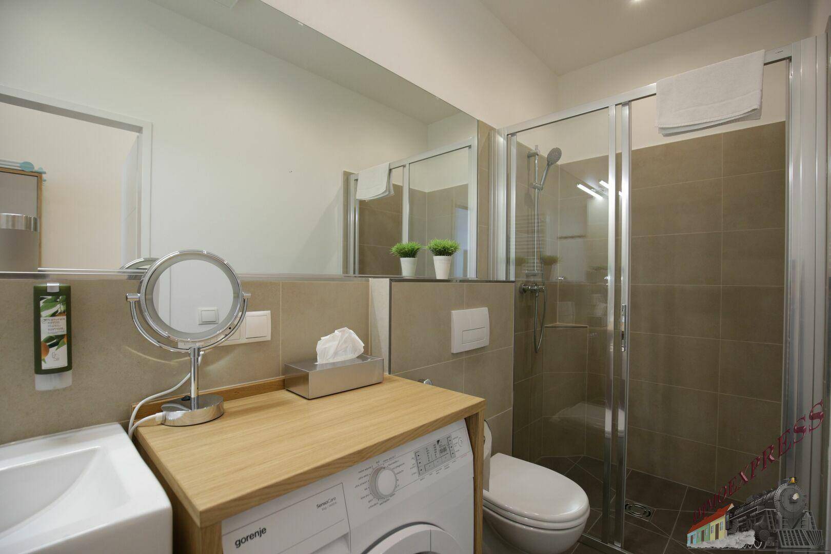 Modernes Badezimmer mit Duschkabine, Waschbecken, Toilette und beigefarbenen Fliesen.