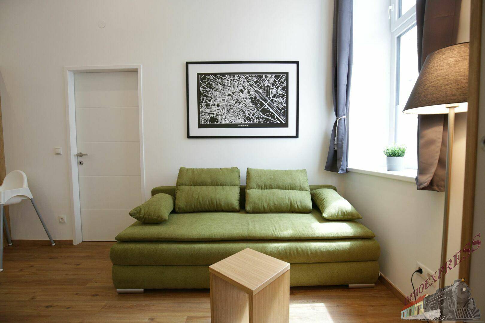 Gemütliches Wohnzimmer mit einem grünen Sofa, Holzboden und einem Fenster.