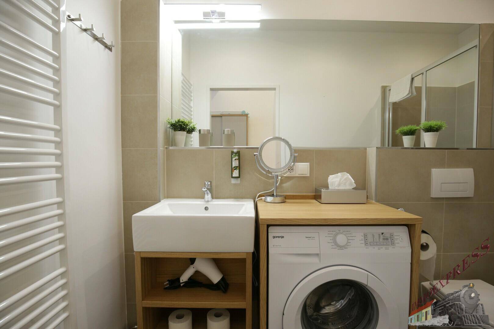 Helles Badezimmer mit Waschbecken, Spiegel und integrierter Waschmaschine unter der Ablage.