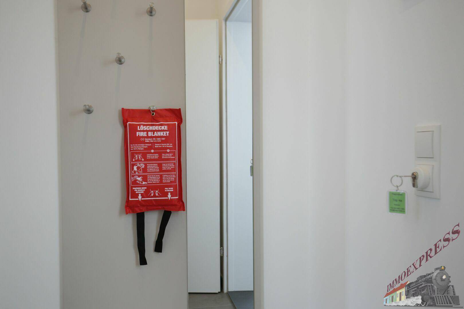 Heller Flur mit Garderobe, einer roten Löschdecke und einem Schlüsselbrett.