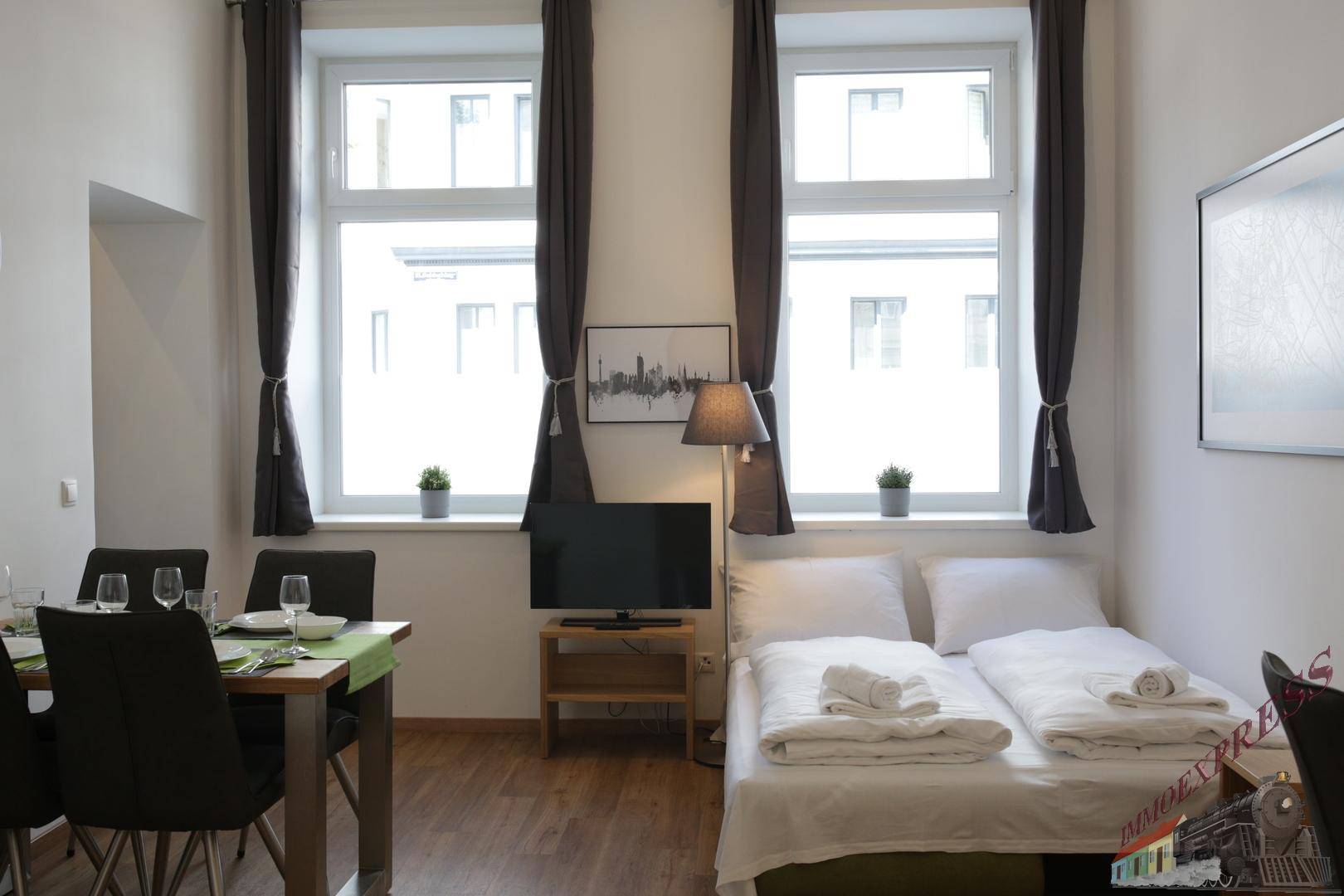 Kombinierter Wohn- und Schlafbereich mit Esstisch, Doppelbett und großen Fenstern.