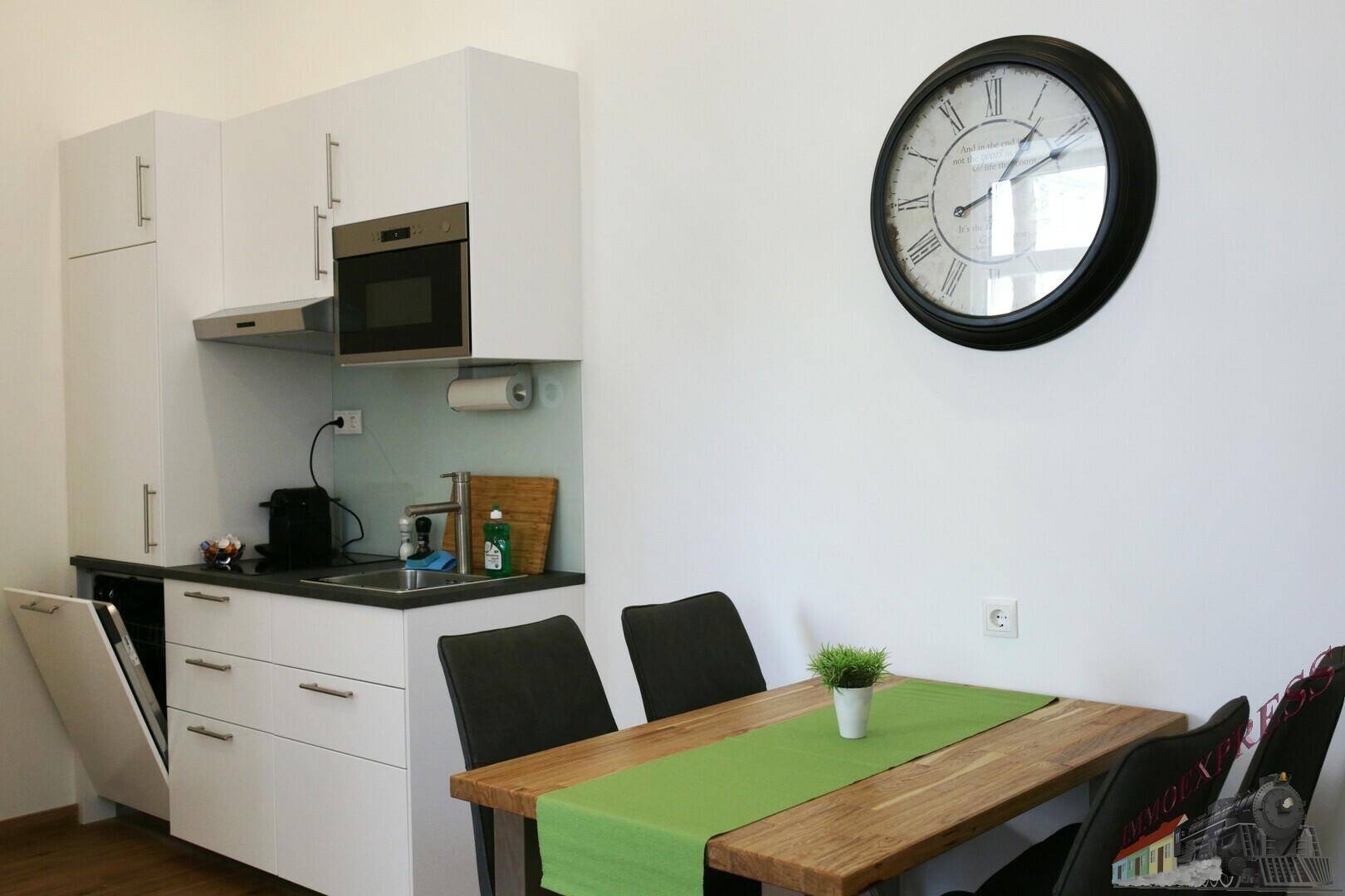Moderne Küchenzeile mit weißen Schränken, integriertem Backofen und einem Esstisch.