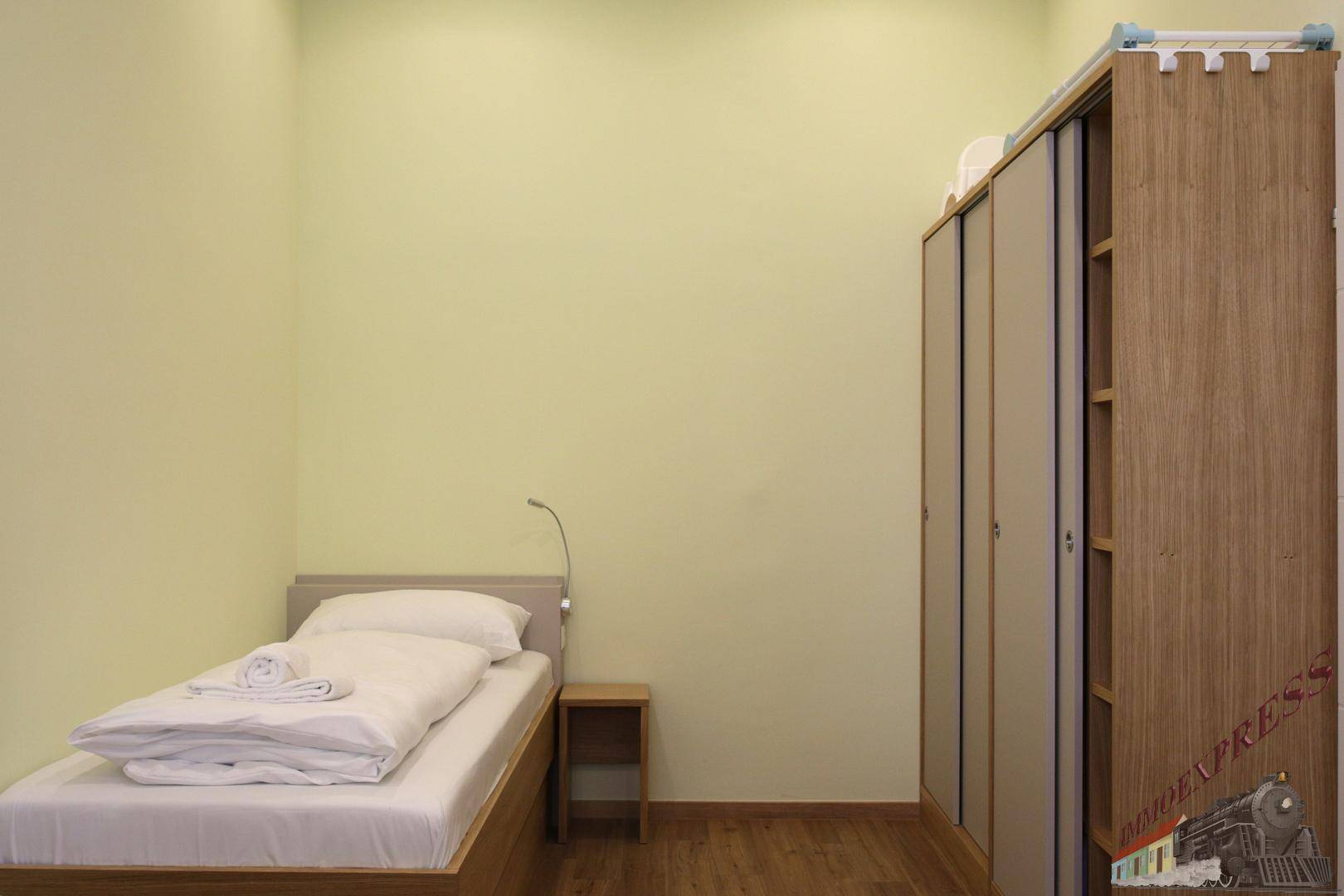 Einzelbett in einem hellen Schlafzimmer mit Holzboden und einem Kleiderschrank.