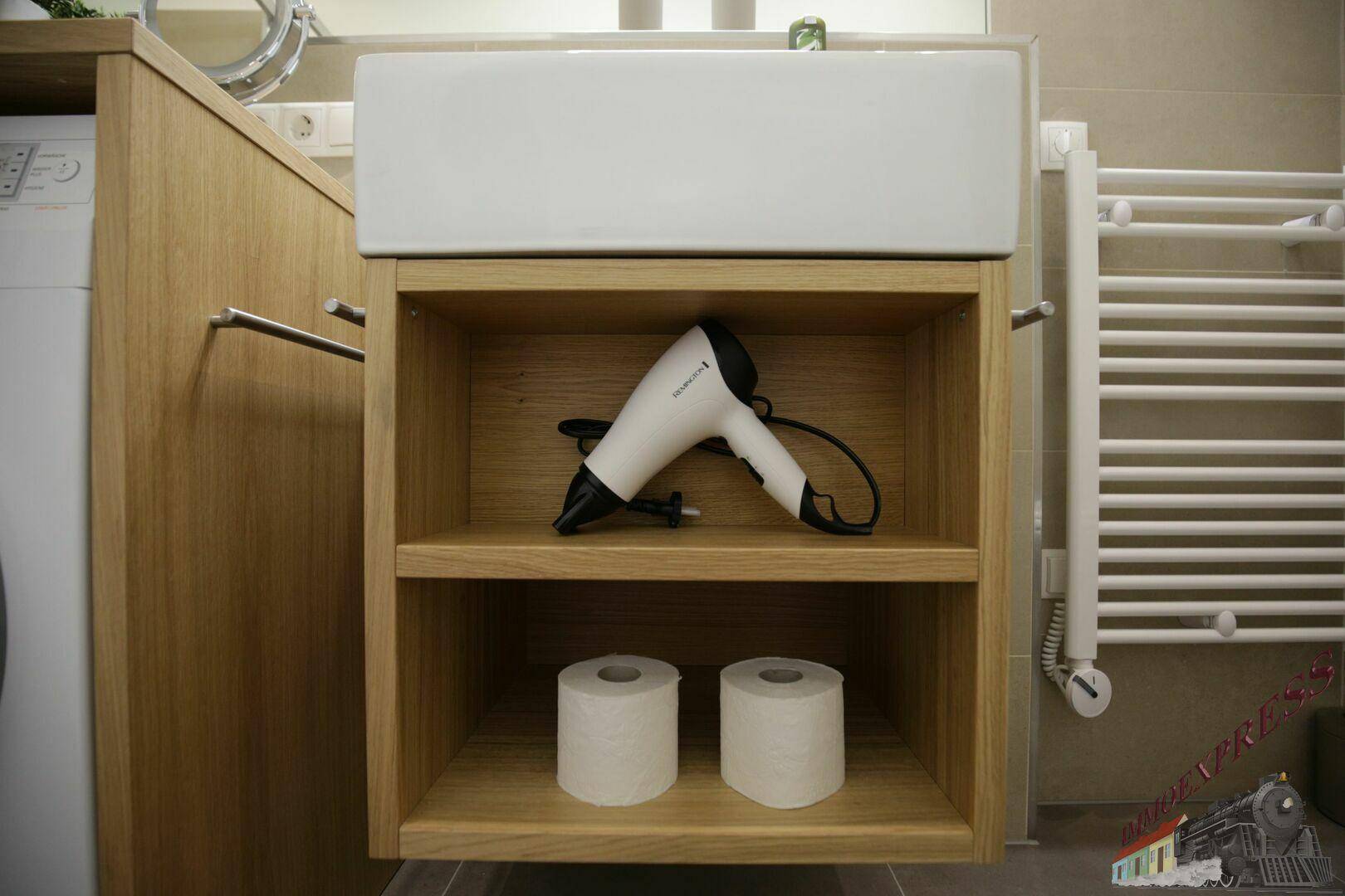 Modernes Badezimmer mit Waschbecken, Holzunterschrank, Föhn und Handtuchheizkörper.