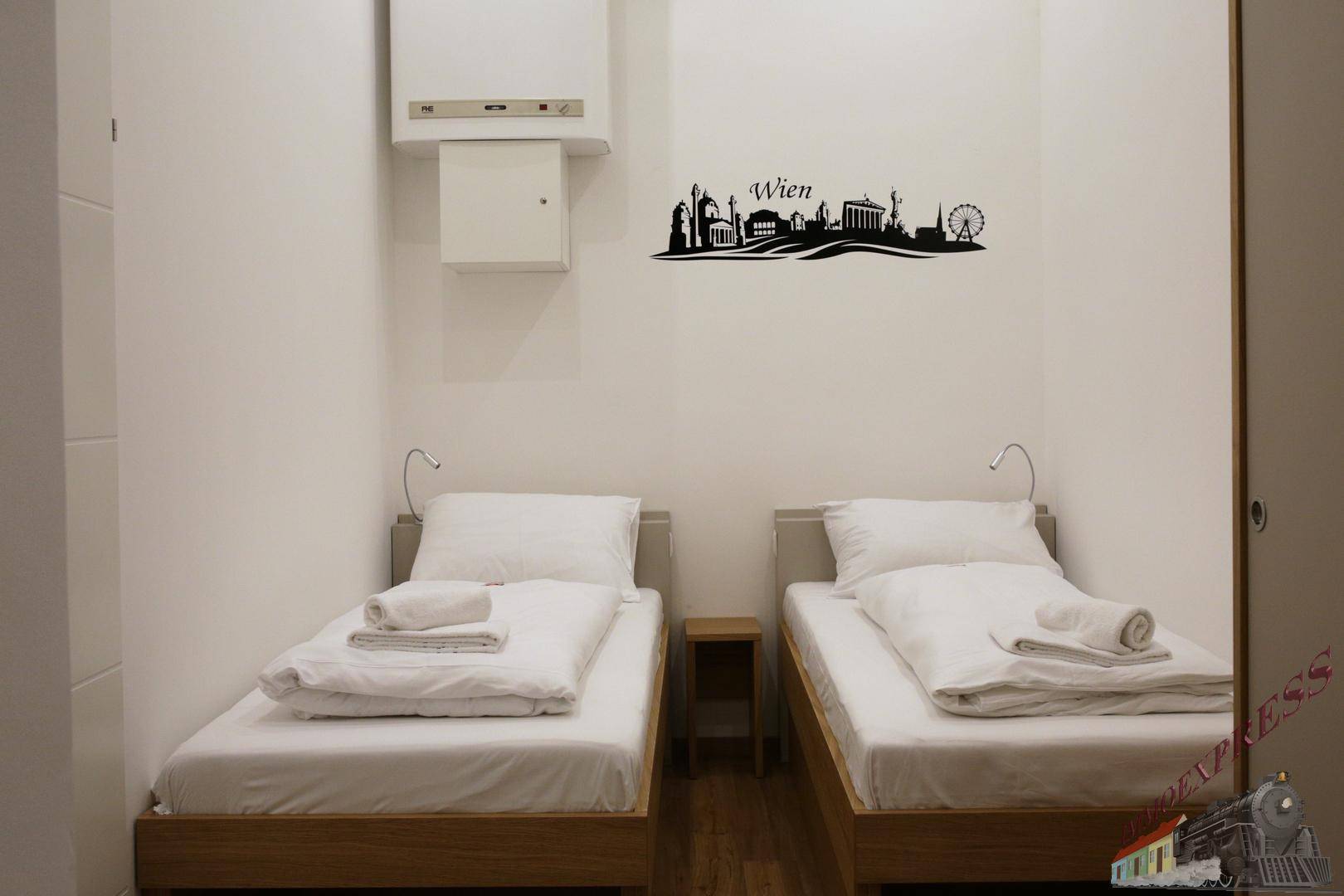 Helles Schlafzimmer mit zwei Einzelbetten, Holzboden und einer Wanddekoration.