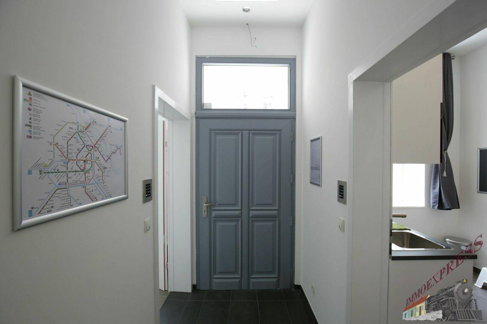 Heller Flur mit dunklem Fliesenboden und einer blaugrauen Eingangstür mit Oberlicht.