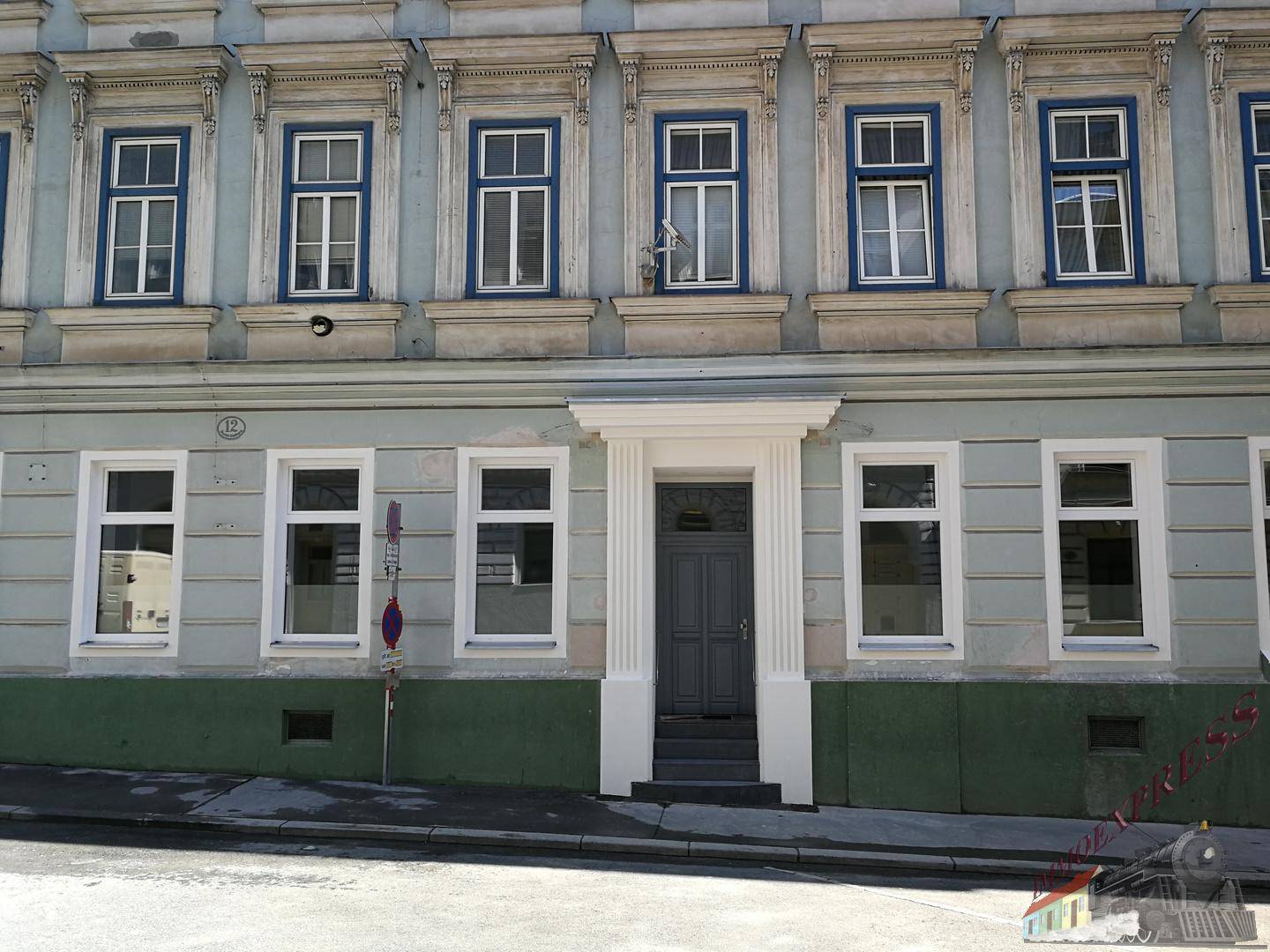 Historische Fassade eines Gebäudes mit blauen Fensterrahmen und einer zentralen Eingangstür.