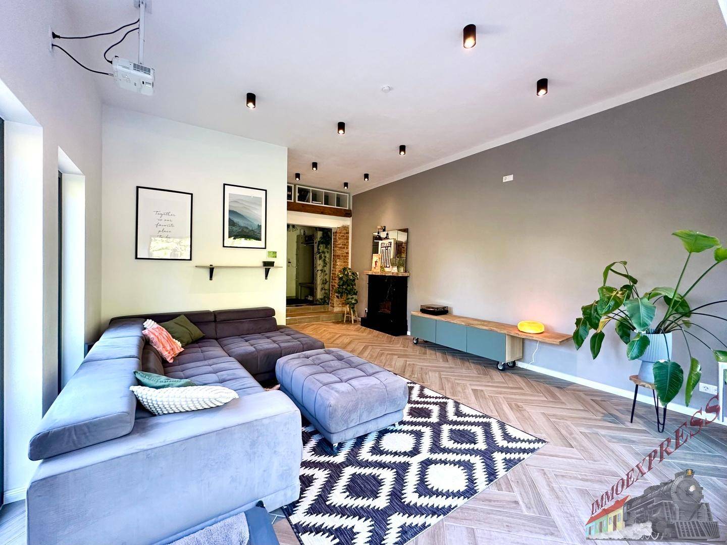 Geräumiges Wohnzimmer mit modernem Sofa, Holzboden und Projektor an der Decke.