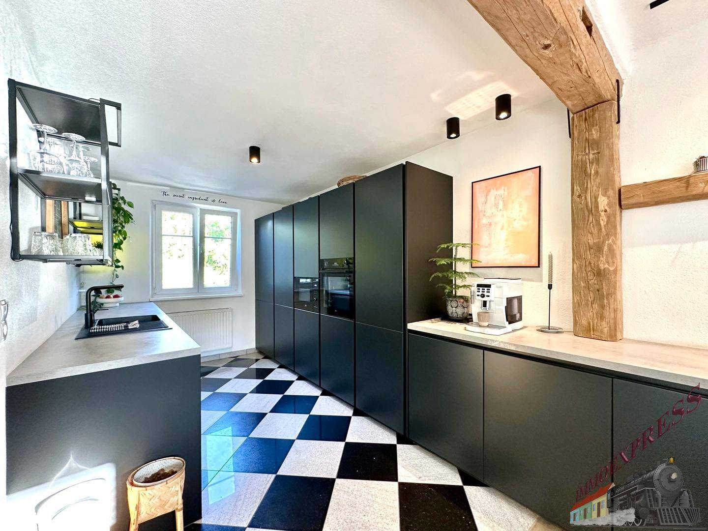 Moderne Küche mit schwarzen Schränken, Schachbrettboden und Holzbalken.