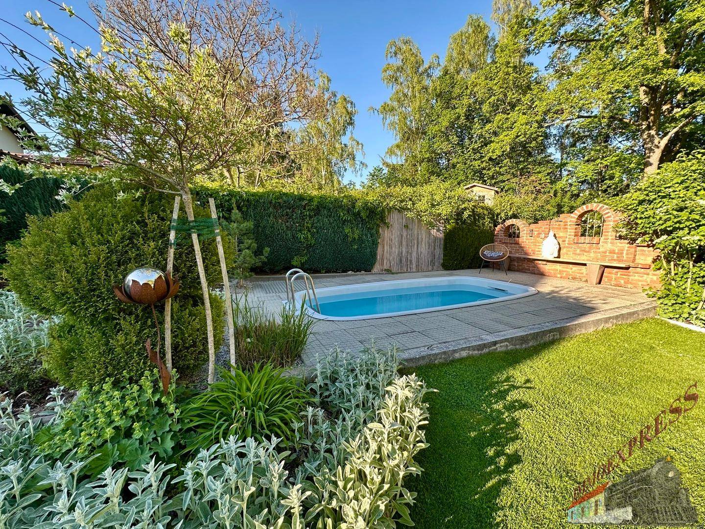 Kleiner Poolbereich im Garten mit Rasenfläche, Hecke und Ziegelmauer.