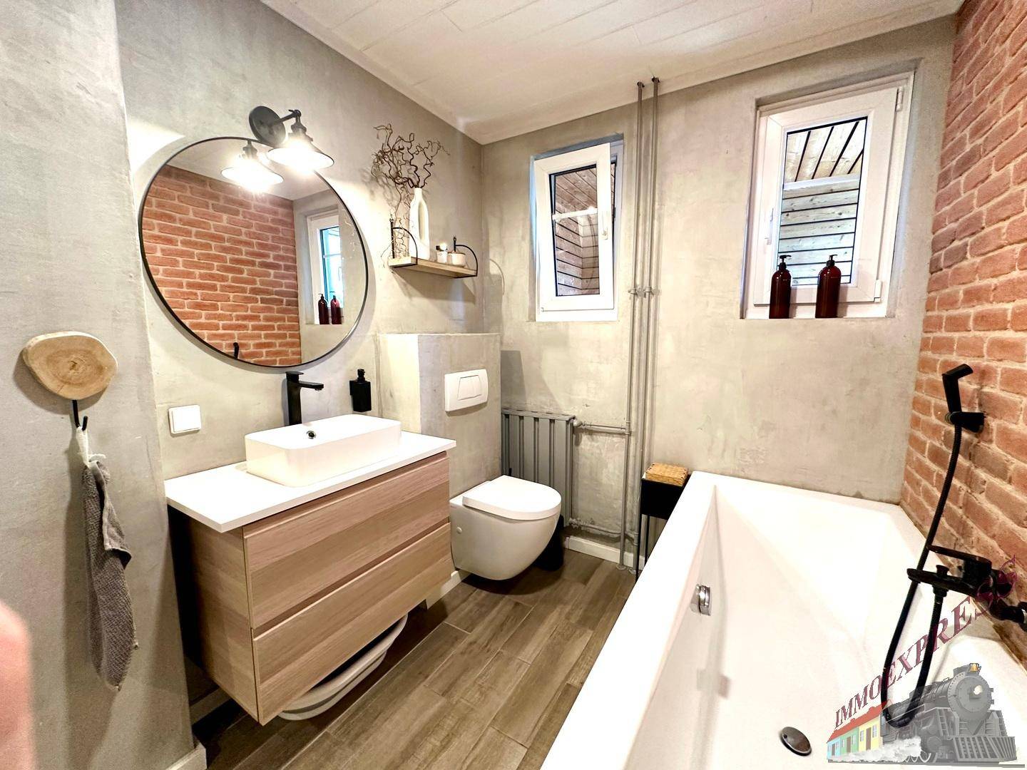 Modernes Badezimmer mit freistehender Badewanne, Waschtisch und unverputzten Ziegelwänden.