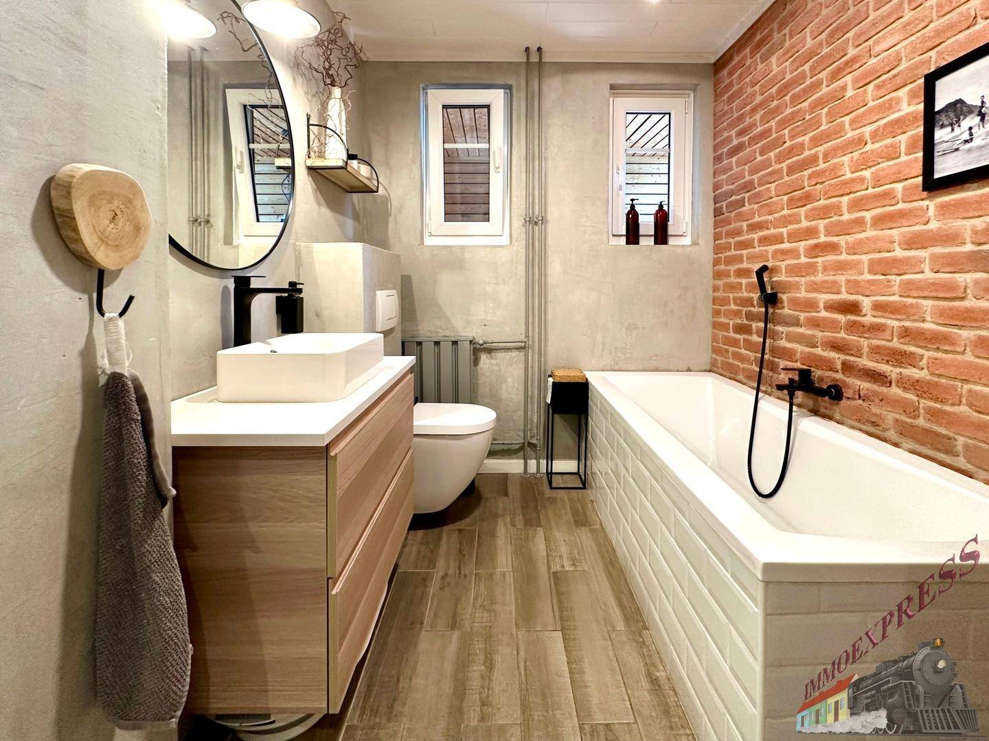 Badezimmer im Industriestil mit Badewanne, Aufsatzwaschbecken und Ziegelwand.