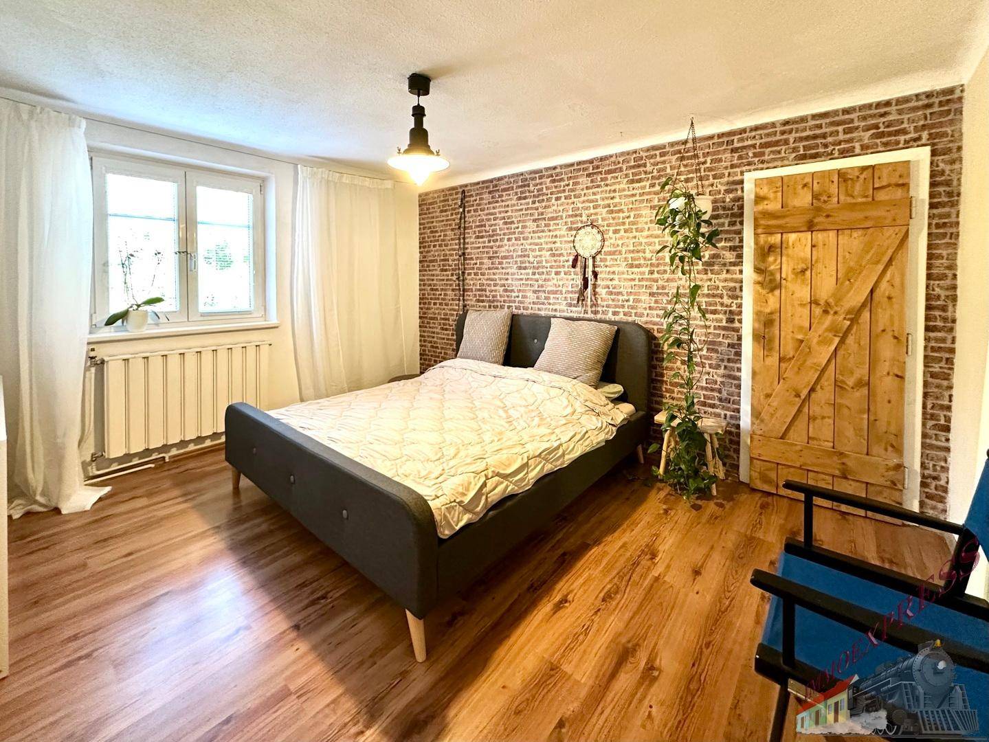 Schlafzimmer mit Holzboden, freiliegender Ziegelwand und rustikaler Schiebetür.