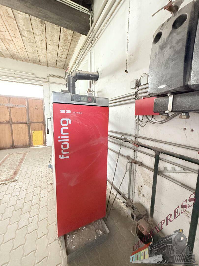 Heizungsraum mit einem modernen Heizkessel, Rohrleitungen und gefliestem Boden.