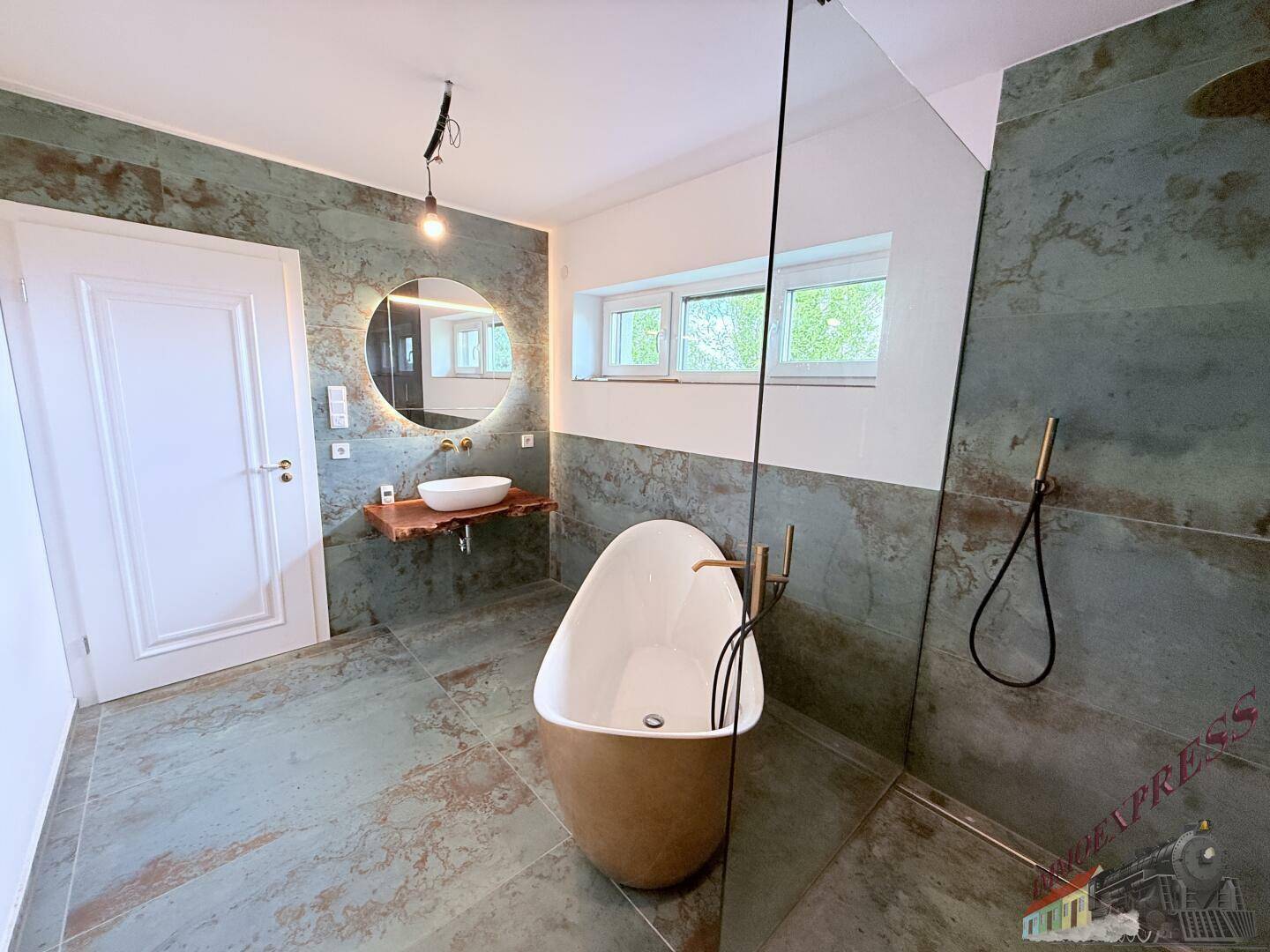 Geräumiges Badezimmer mit runder Spiegelleuchte, freistehender Badewanne und großer begehbarer Dusche.