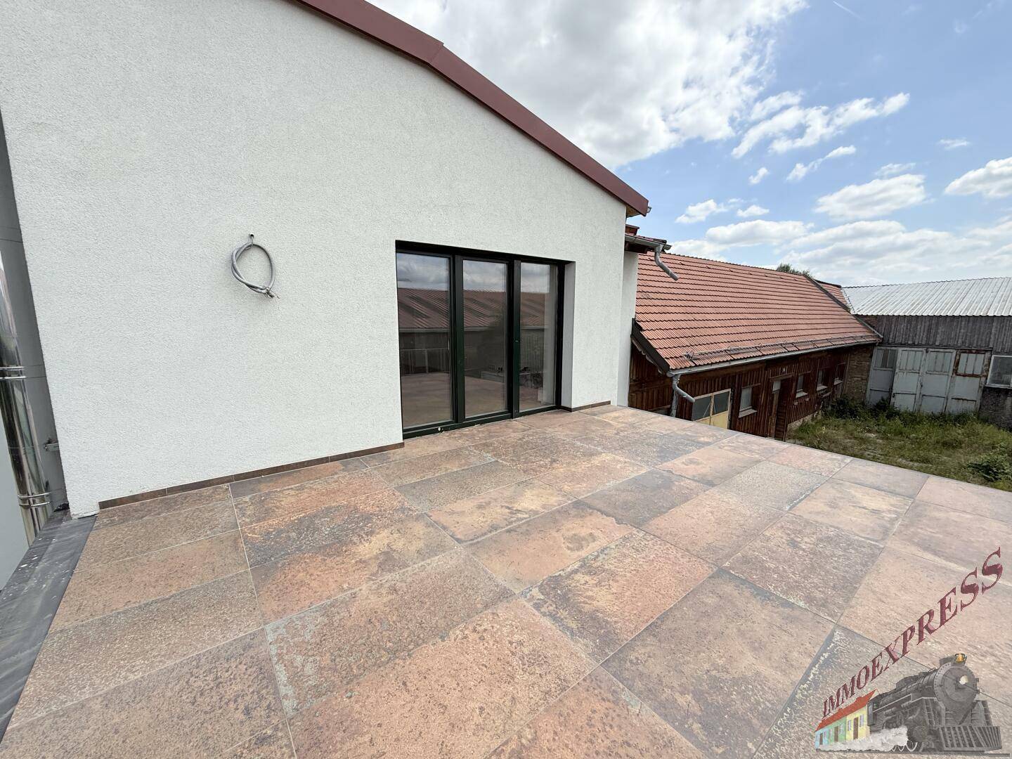 Geräumige, geflieste Dachterrasse mit moderner Schiebetür und Blick auf die Umgebung.