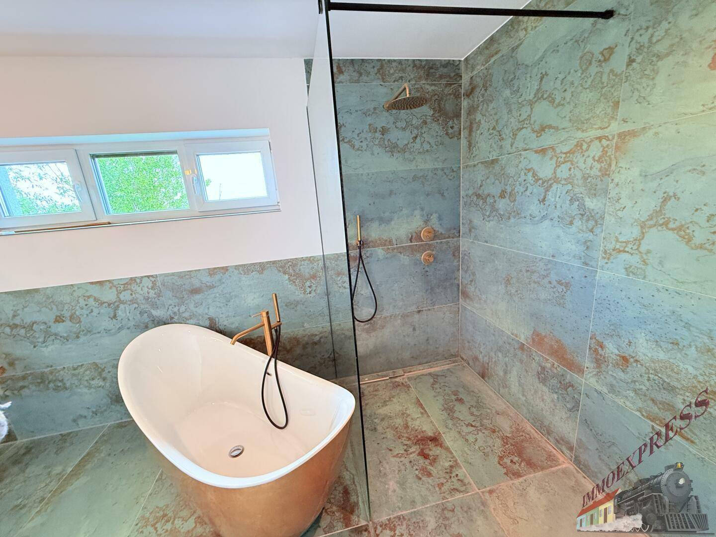 Elegantes Badezimmer mit freistehender Badewanne, begehbarer Dusche und Fenster, ausgestattet mit goldenen Armaturen.