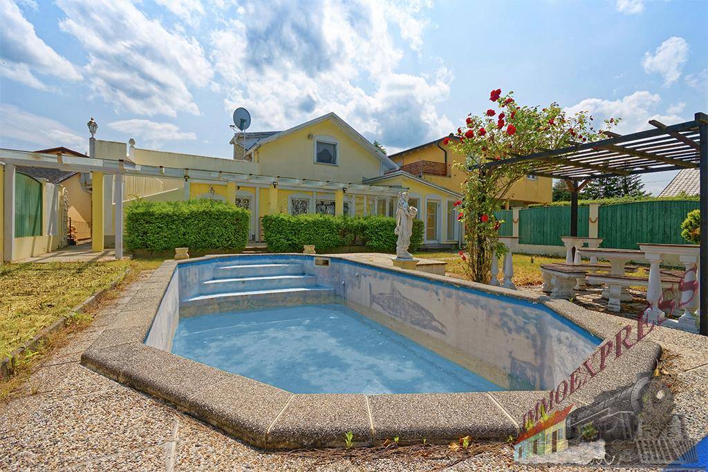 Hinterhof mit Pool und gelbem Haus im Hintergrund, umgeben von Hecken und einer Pergola.