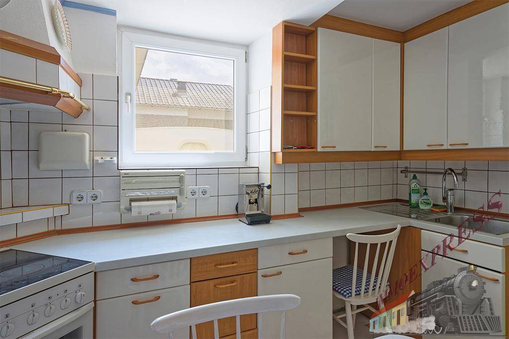 Funktionale Küche mit weißen Fliesen, Holzdetails und Fenster mit Blick nach draußen.