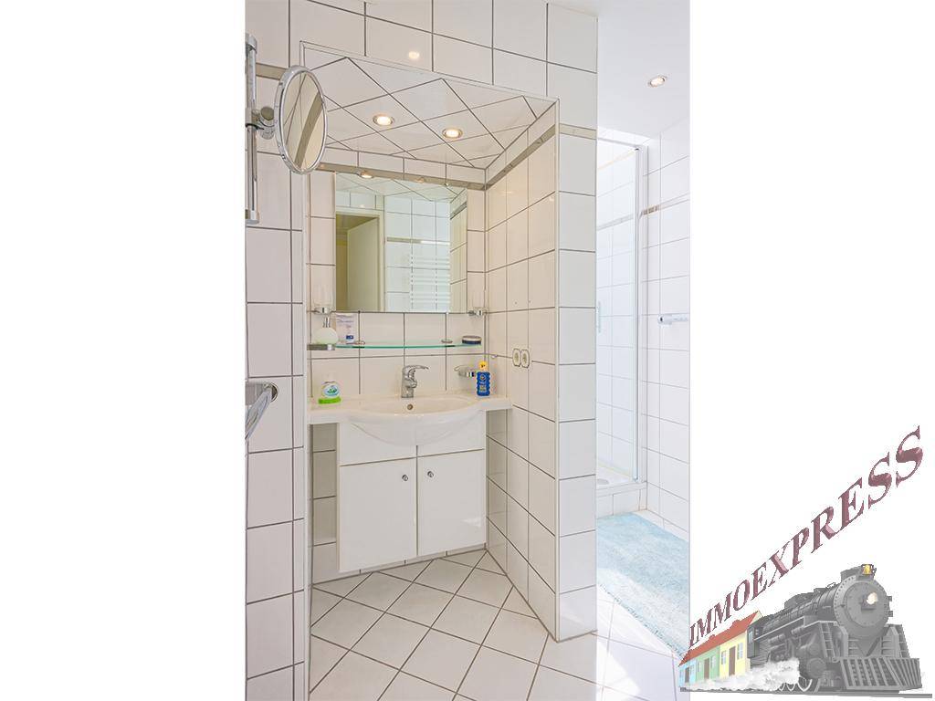 Badezimmer mit Waschbecken, Spiegel und weißen Fliesen, ausgestattet mit praktischen Details.