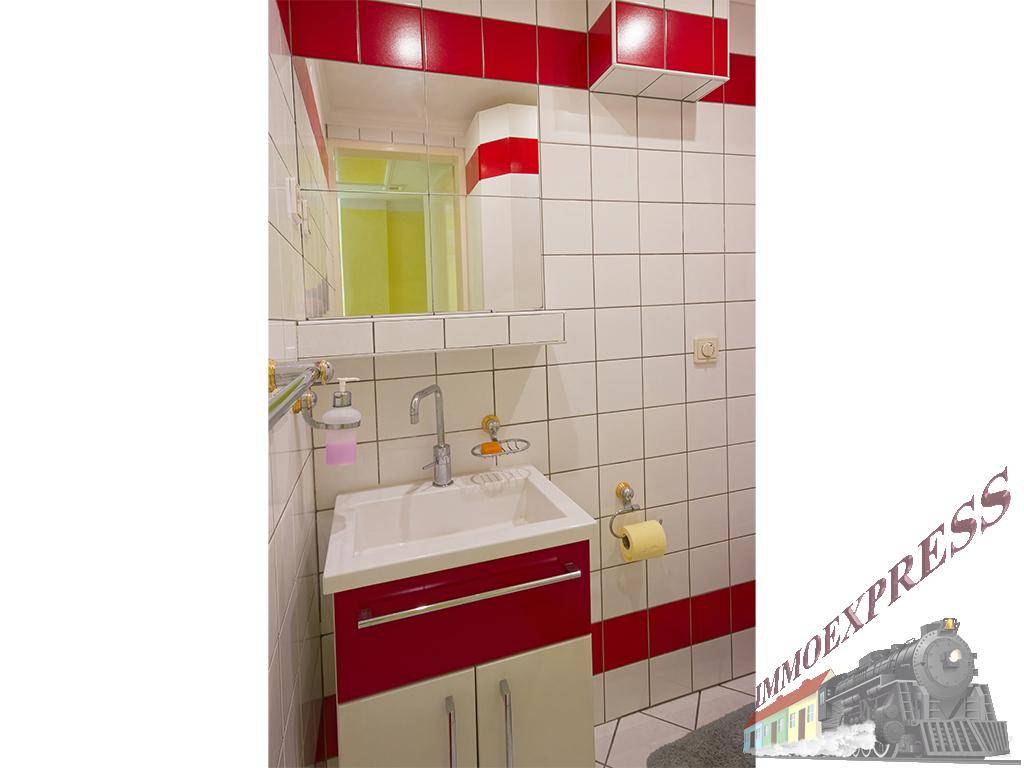 Kleines Badezimmer mit Waschbecken, Spiegel und roten Akzentfliesen, funktional gestaltet.