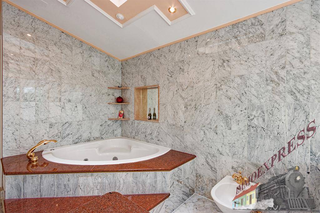 Luxuriöses Badezimmer mit Eckbadewanne, Marmorfliesen und goldfarbenen Armaturen.