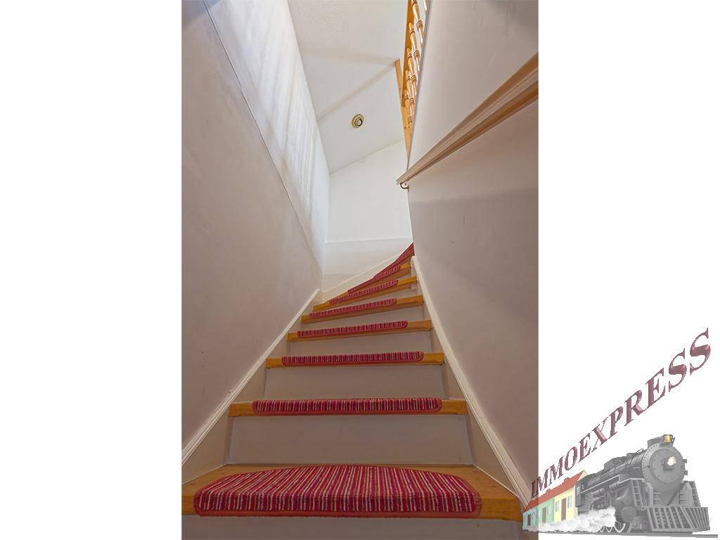 Treppenhaus mit Holzstufen und rotem Teppichläufer, der in die obere Etage führt.