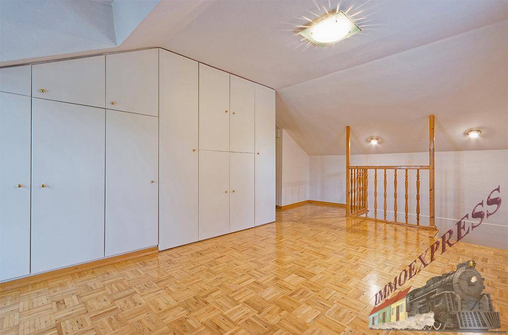 Geräumiges Dachzimmer mit Einbauschränken, Parkettboden und Holzgeländer.