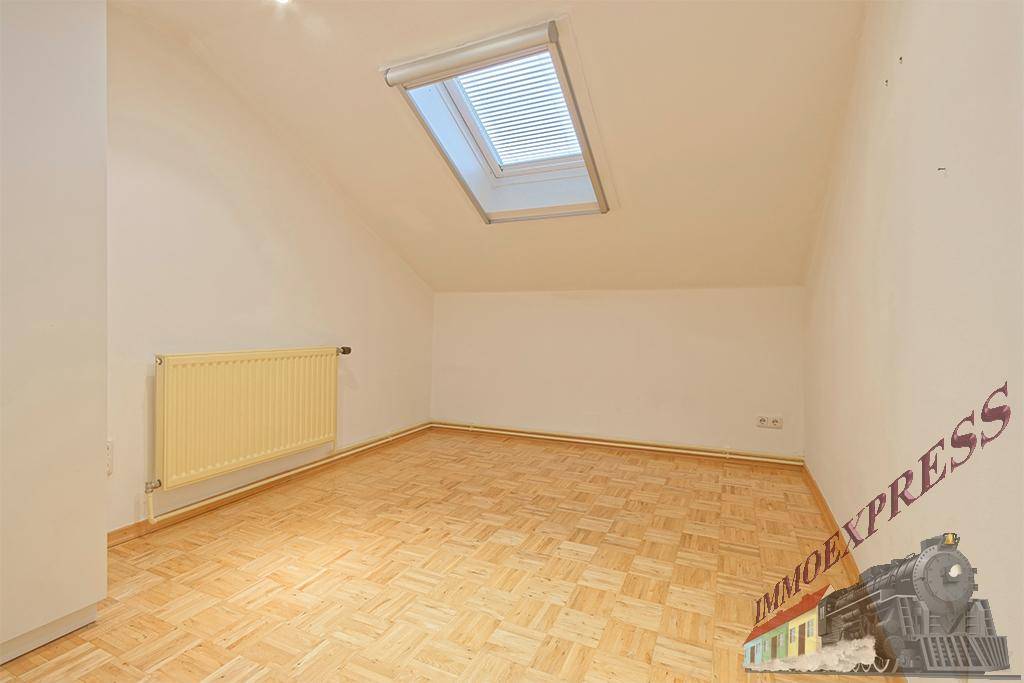 Helles Dachzimmer mit Parkettboden, Heizkörper und Dachfenster für natürliches Licht.