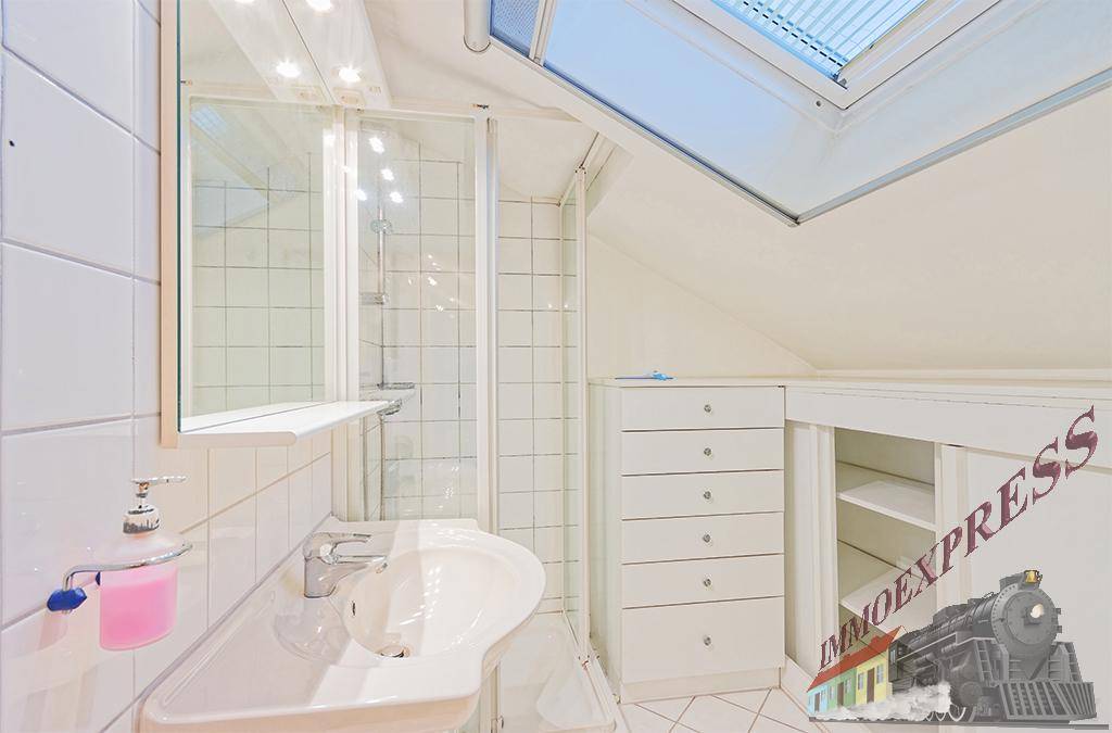 Helles Badezimmer im Dachgeschoss mit Dusche, Waschbecken und Dachfenster für natürliches Licht.