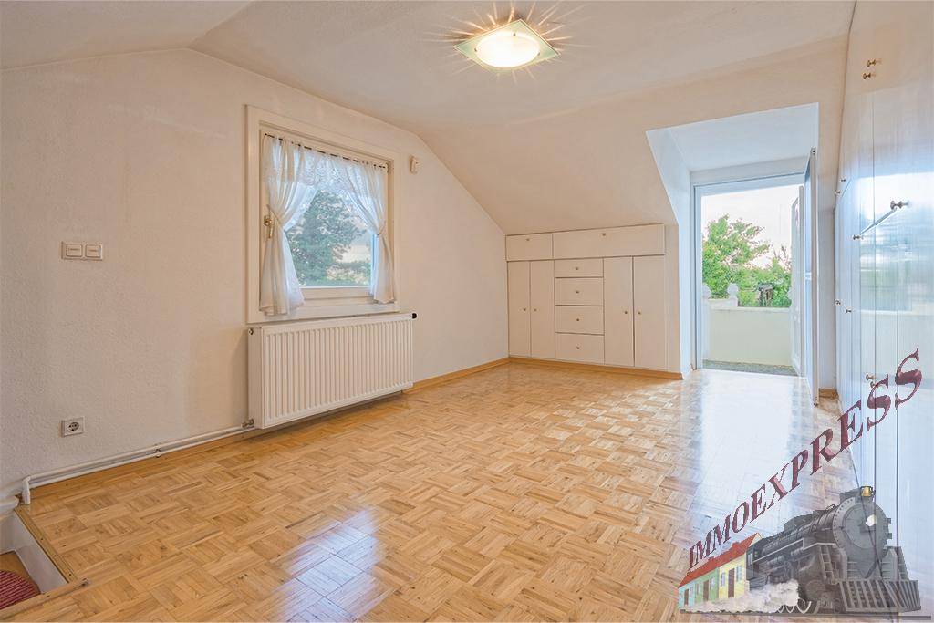 Geräumiges Zimmer im Dachgeschoss mit Parkettboden, Einbauschränken und Zugang zum Außenbereich.