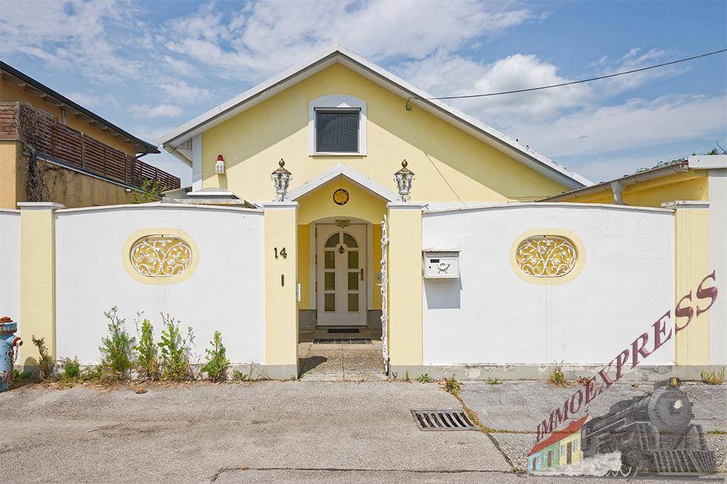Gelbe Hausfassade mit weißer Mauer, dekorativen Elementen und einem einladenden Eingangsbereich.