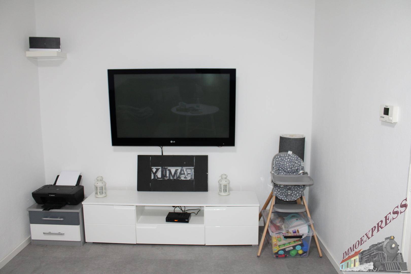 Wohnbereich mit großem Wandfernseher, weißem TV-Möbel und minimalistischer Dekoration.