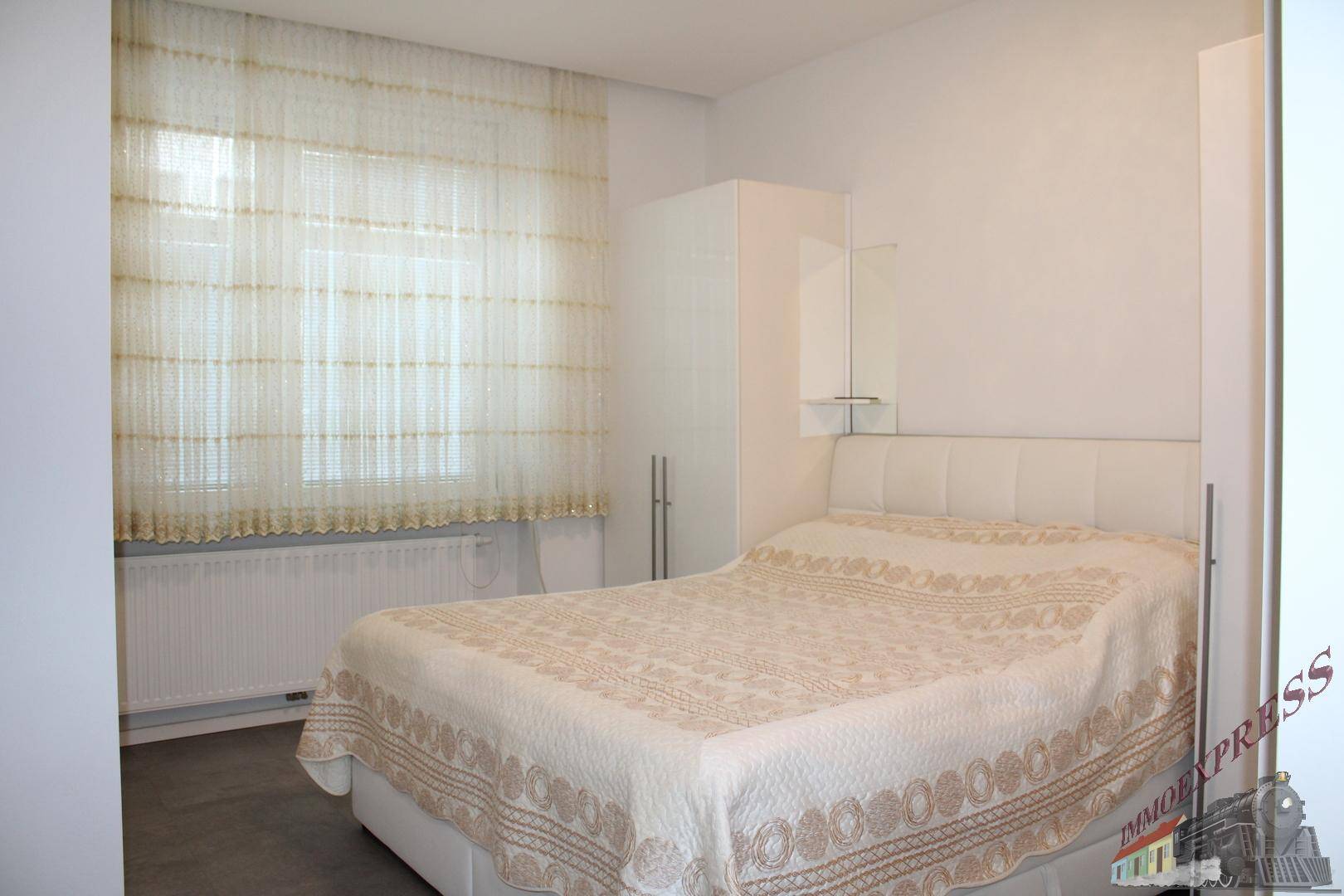 Gemütliches Schlafzimmer mit Doppelbett, weißem Kopfteil und Vorhängen am Fenster.