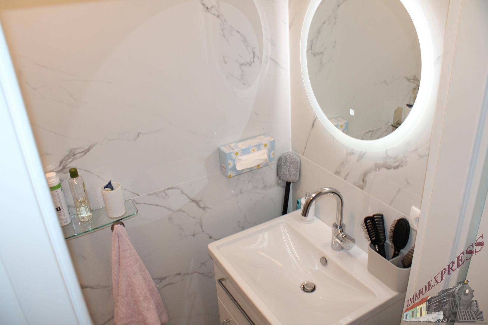 Modernes Gäste-WC mit kleinem Waschbecken und beleuchtetem Spiegel, elegant gefliest.