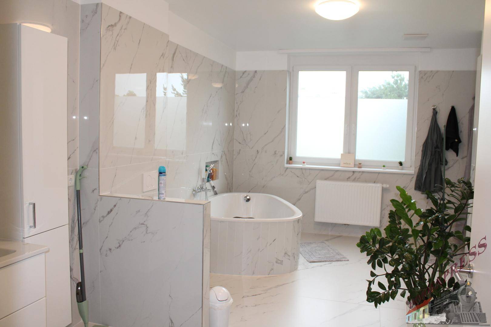 Geräumiges Badezimmer mit großer Badewanne, Marmorfliesen und Fenster für natürliches Licht.