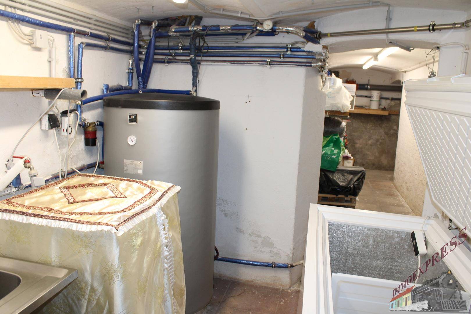 Technikraum im Keller mit Warmwasserspeicher, Rohrleitungen und Gefrierschrank.