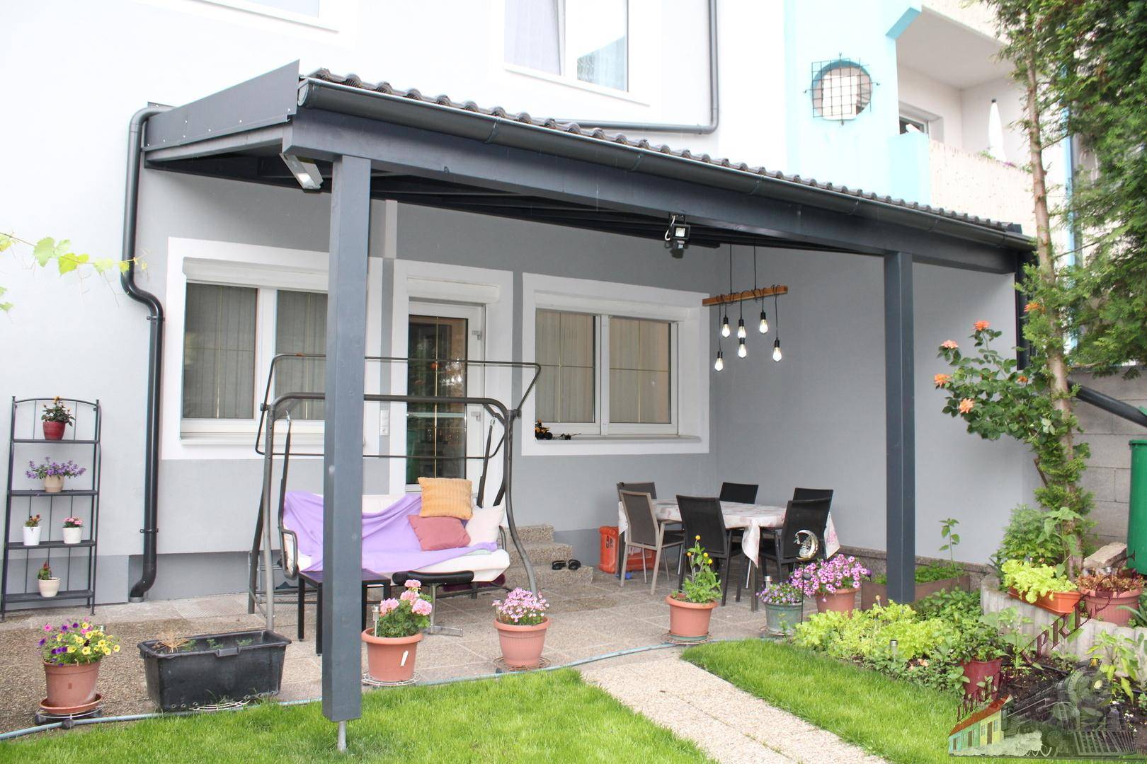 Überdachte Terrasse mit Sitzgelegenheiten, Schaukel und Topfpflanzen, ideal für entspannte Stunden im Freien.