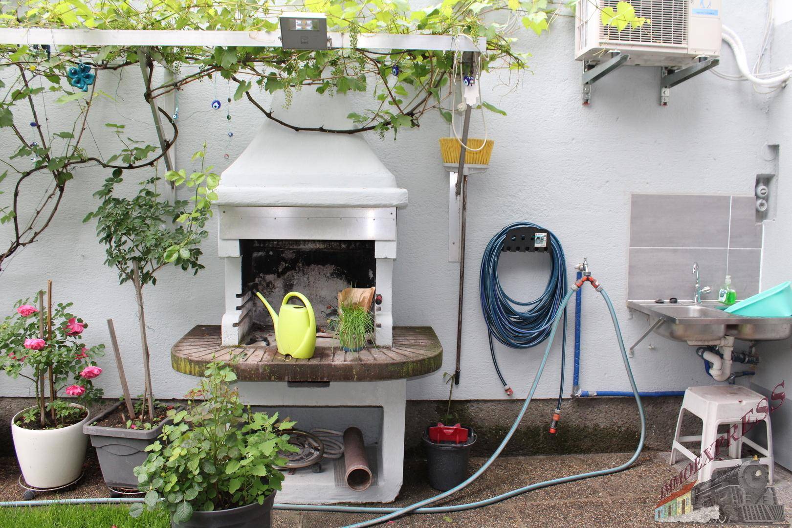 Gemütlicher Grillbereich im Freien mit eingebautem Grill und Spülbecken, umgeben von Pflanzen.