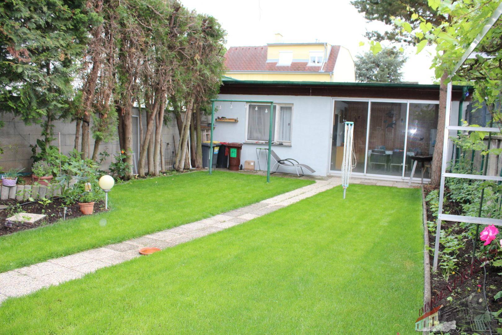 Langer, schmaler Gartenbereich mit Rasenfläche und einem kleinen Nebengebäude im Hintergrund.